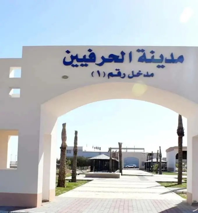 The gateway to Craftsmen City in Hurghada: a pale archway signed in Arabic "Craftsmen City, Entrance No. 1" over a paved walkway lined with palms, with low buildings behind.