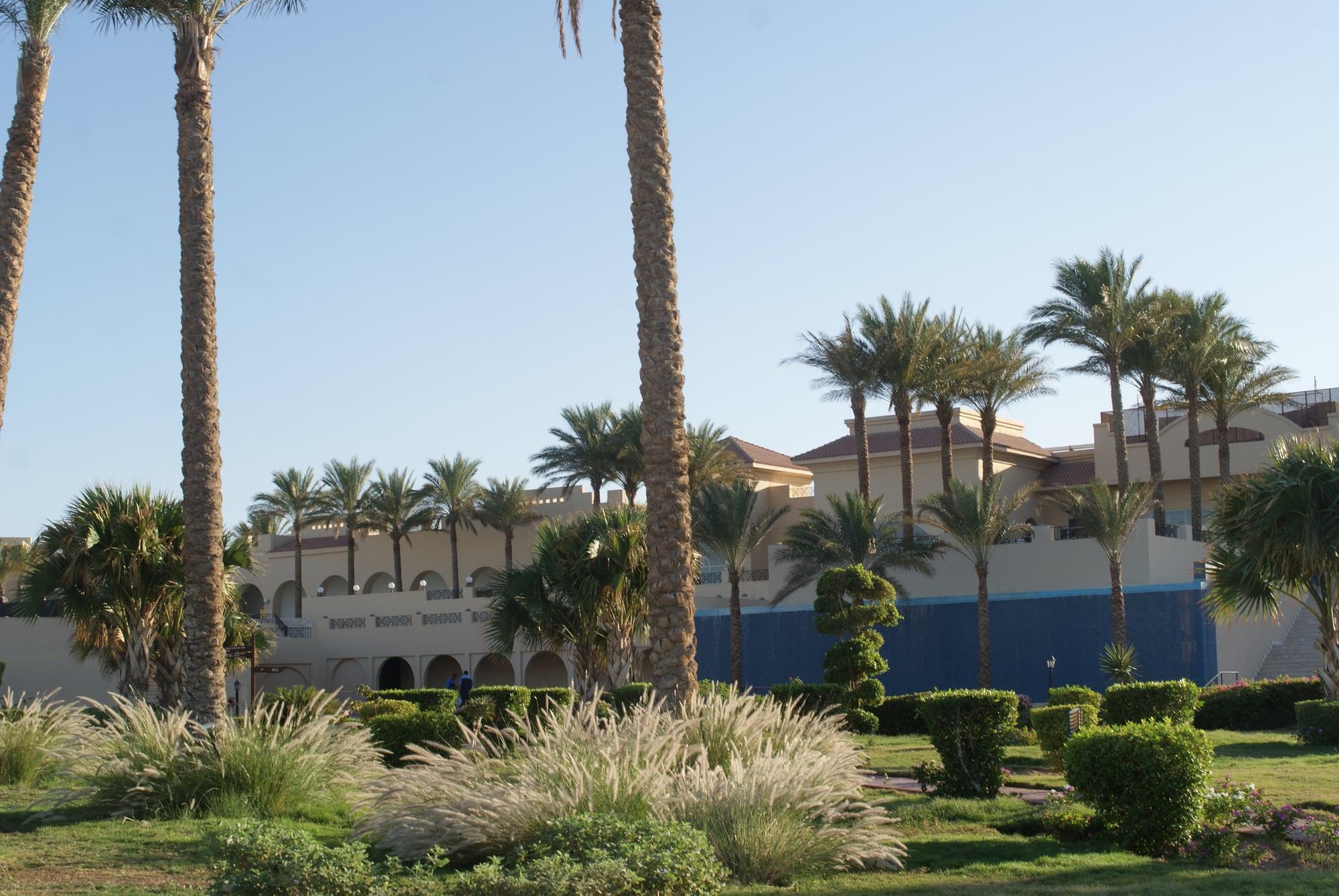 Landscaped resort gardens with palms and clipped hedges in front of an arcaded hotel at Makadi Bay