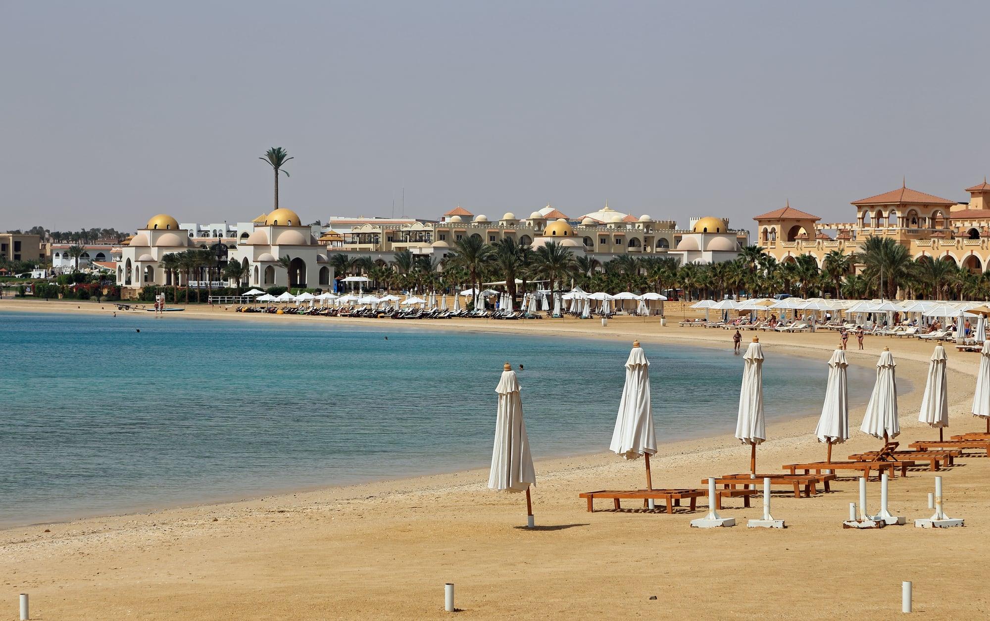 A calm turquoise bay at Sahl Hasheesh, white beach parasols in front of domed resort buildings
